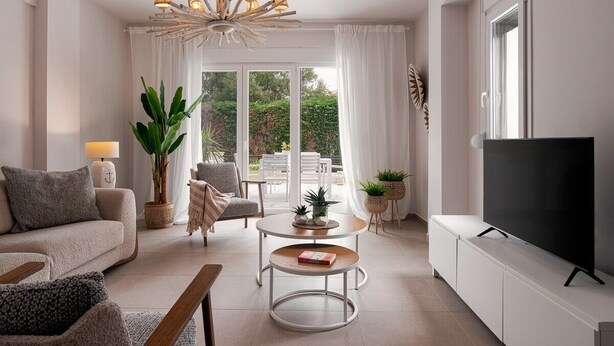 A modern living room with a sofa, coffee table, TV, and a large window with curtains. - Paradise Overlook - Beachfront Villa (Pefkohori)