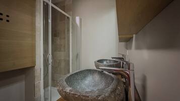 Une salle de bain avec un lavabo en pierre, une douche et des meubles en bois.