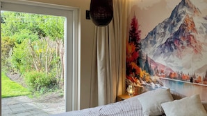 A bedroom with a bed, a hanging light fixture, a window, and a mural of mountains.