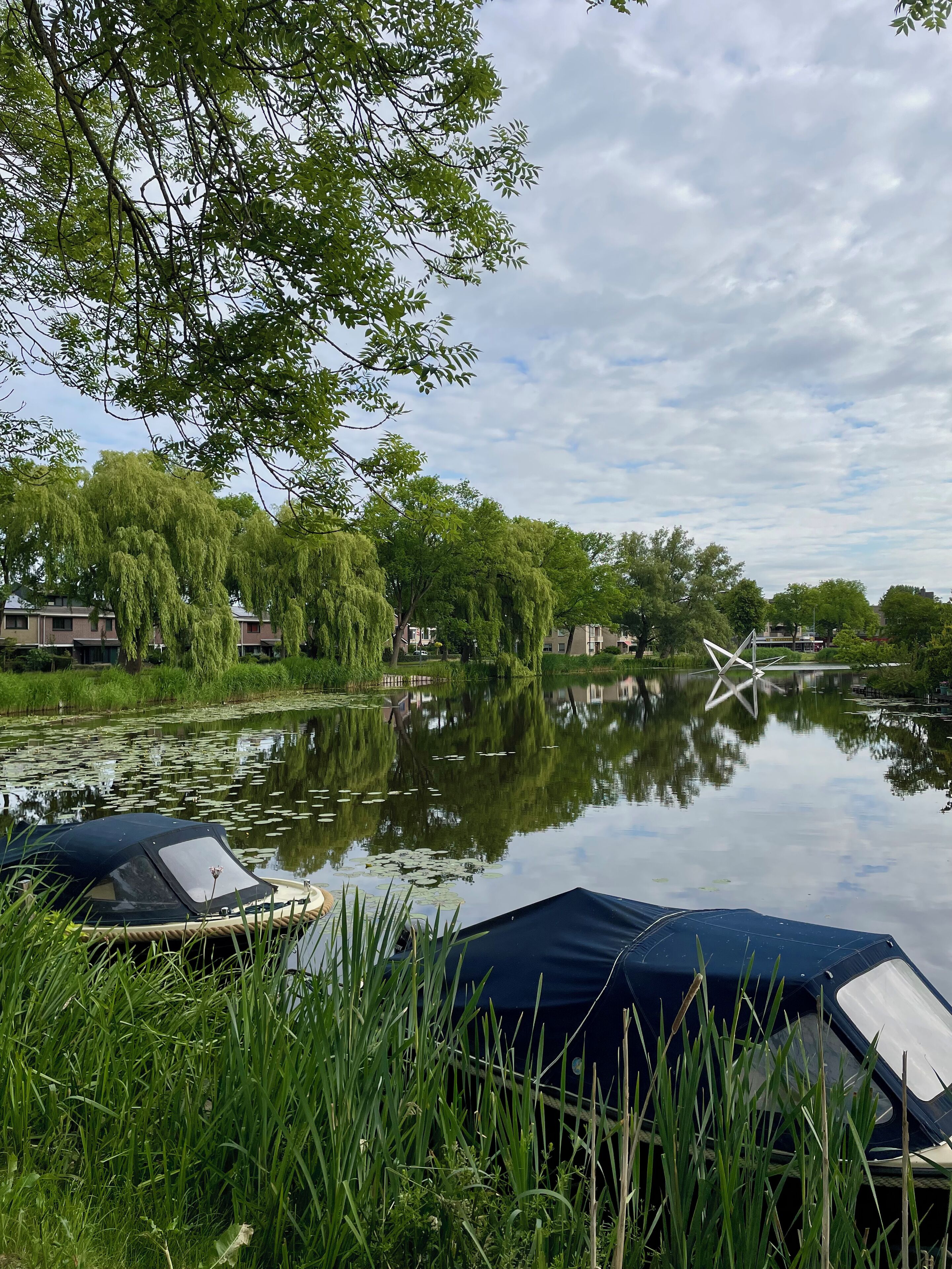 A serene lakeside view with boats, lush greenery, and a clear sky.
