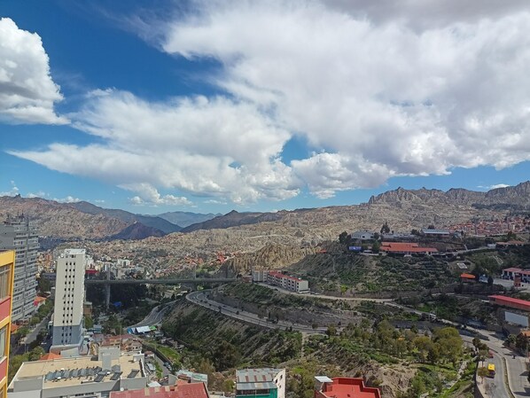 A cityscape with a prominent building, a bridge, and mountainous terrain in the background.