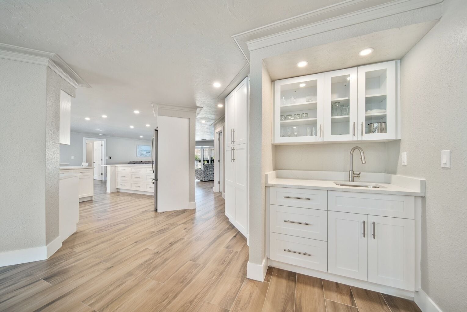 Une cuisine moderne avec des meubles blancs, un évier en acier inoxydable et un plancher en bois.