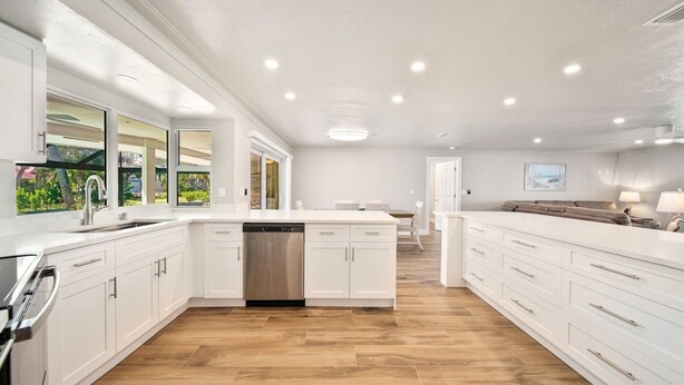 Une cuisine spacieuse avec des meubles blancs, un lave-vaisselle et un plancher en bois.