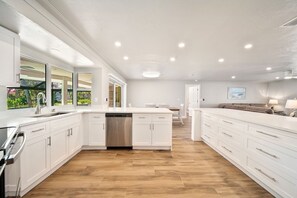 Una cocina amplia con armarios blancos, lavavajillas y suelo de madera.