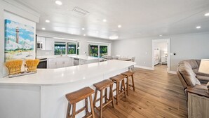 Une cuisine moderne dotée d’un grand îlot central, de tabourets de bar en bois et d’un tableau représentant un phare.