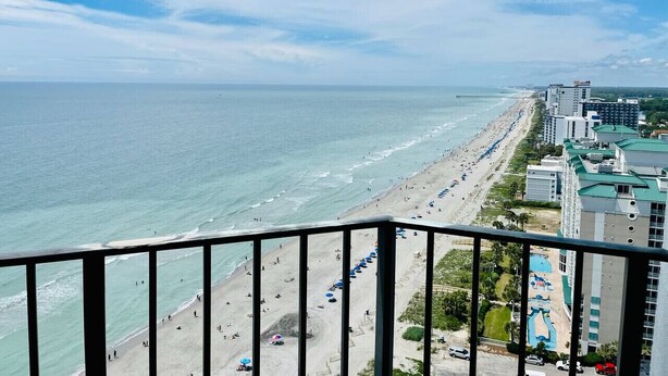 A coastal hotel with a beach view, multiple swimming pools, and a long promenade along the shore.