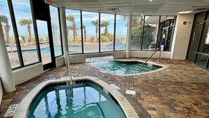 An indoor swimming pool with clear views of palm trees and a beach through large windows.