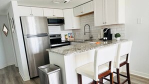 A modern kitchen with white cabinets, stainless steel appliances, a granite countertop, and wooden bar stools.