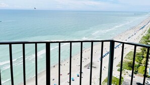 A beach view from a balcony with a railing, ocean, and beachgoers.