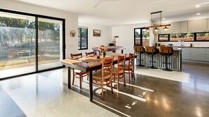 Una cocina moderna con una isla grande, un comedor con mesa y sillas de madera, y grandes puertas correderas de vidrio que dan a un patio trasero.