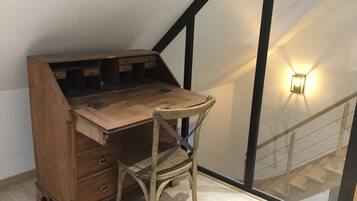 A corner desk with drawers and a chair, positioned next to a glass railing and a wall-mounted light fixture.