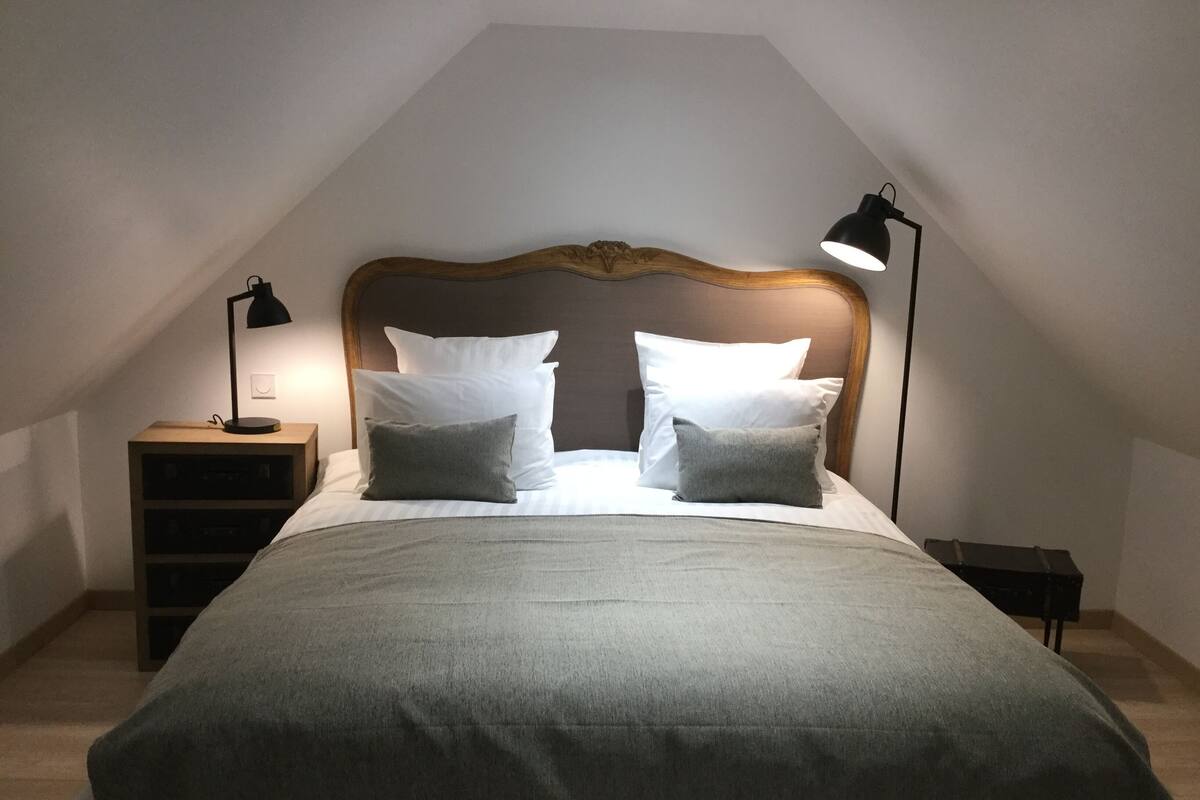 A neatly made bed with a wooden headboard, two bedside lamps, and a small nightstand.