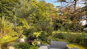 A garden patio with wicker furniture and a small table, surrounded by gravel and various plants. - Auberge de keranden (Landerneau)