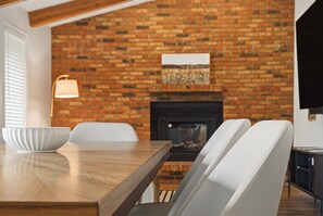 A dining area with a brick wall, a fireplace, and a modern light fixture. - Galena Home with Golf Course View (Galena)