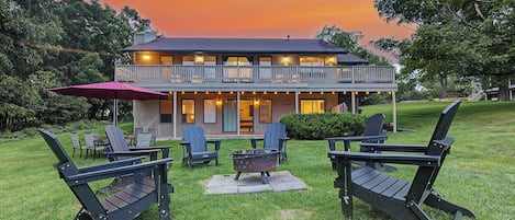 A two-story house with a balcony, outdoor seating area with Adirondack chairs, and a fire pit.