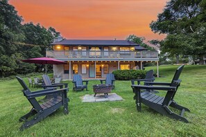 Una casa de dos pisos con un balcón, un área de estar exterior con sillas tipo Adirondack y una chimenea.