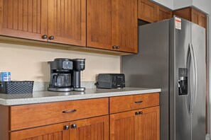 A kitchen with wooden cabinets, a stainless steel refrigerator, a coffee maker, and a toaster.