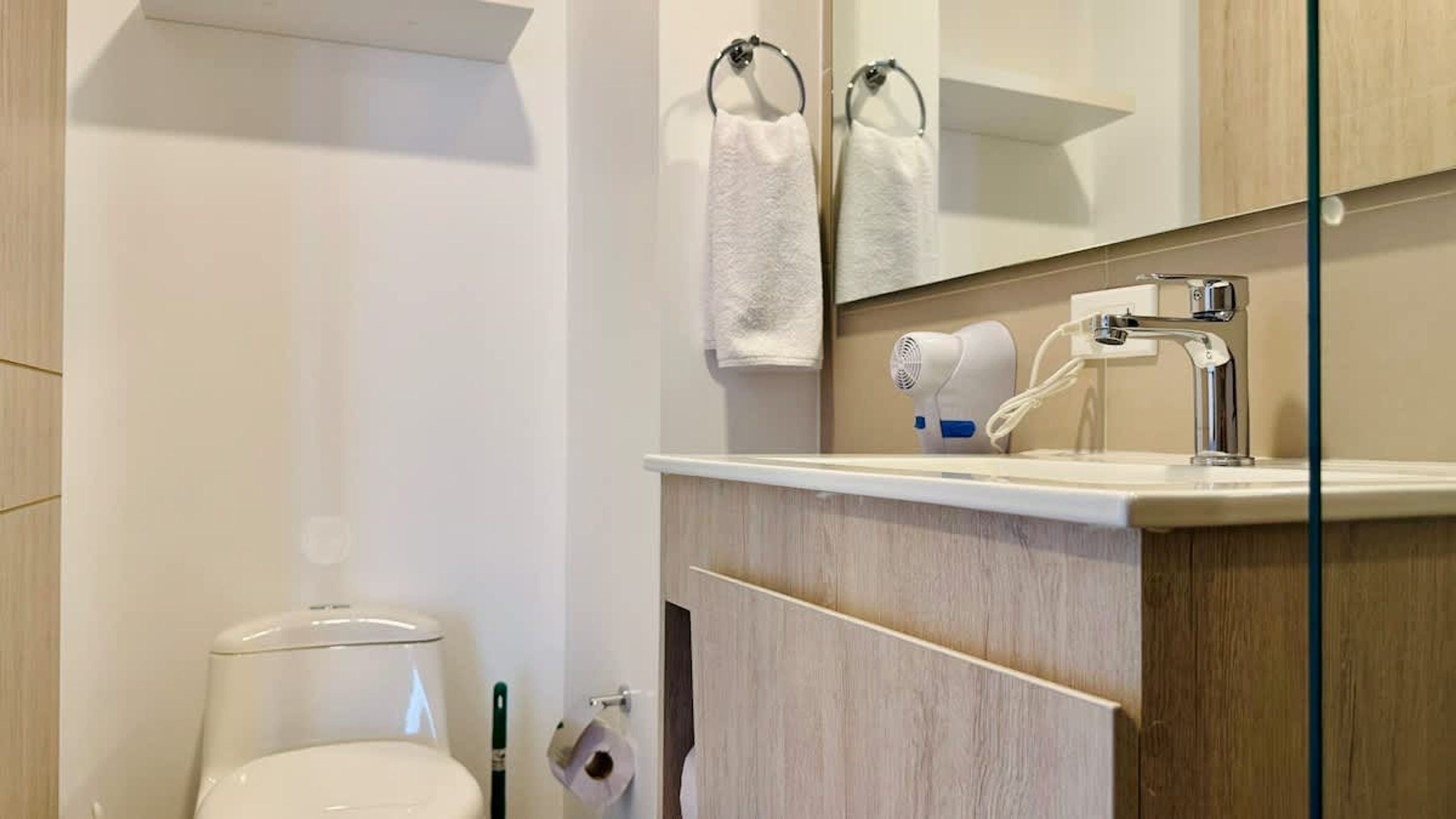 A modern bathroom with a toilet, a sink with a towel hanging on the wall, and a hairdryer on the counter.
