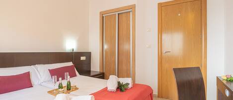 A hotel room with two beds, a wooden wardrobe, a desk with a chair, and a tray with glasses and snacks.