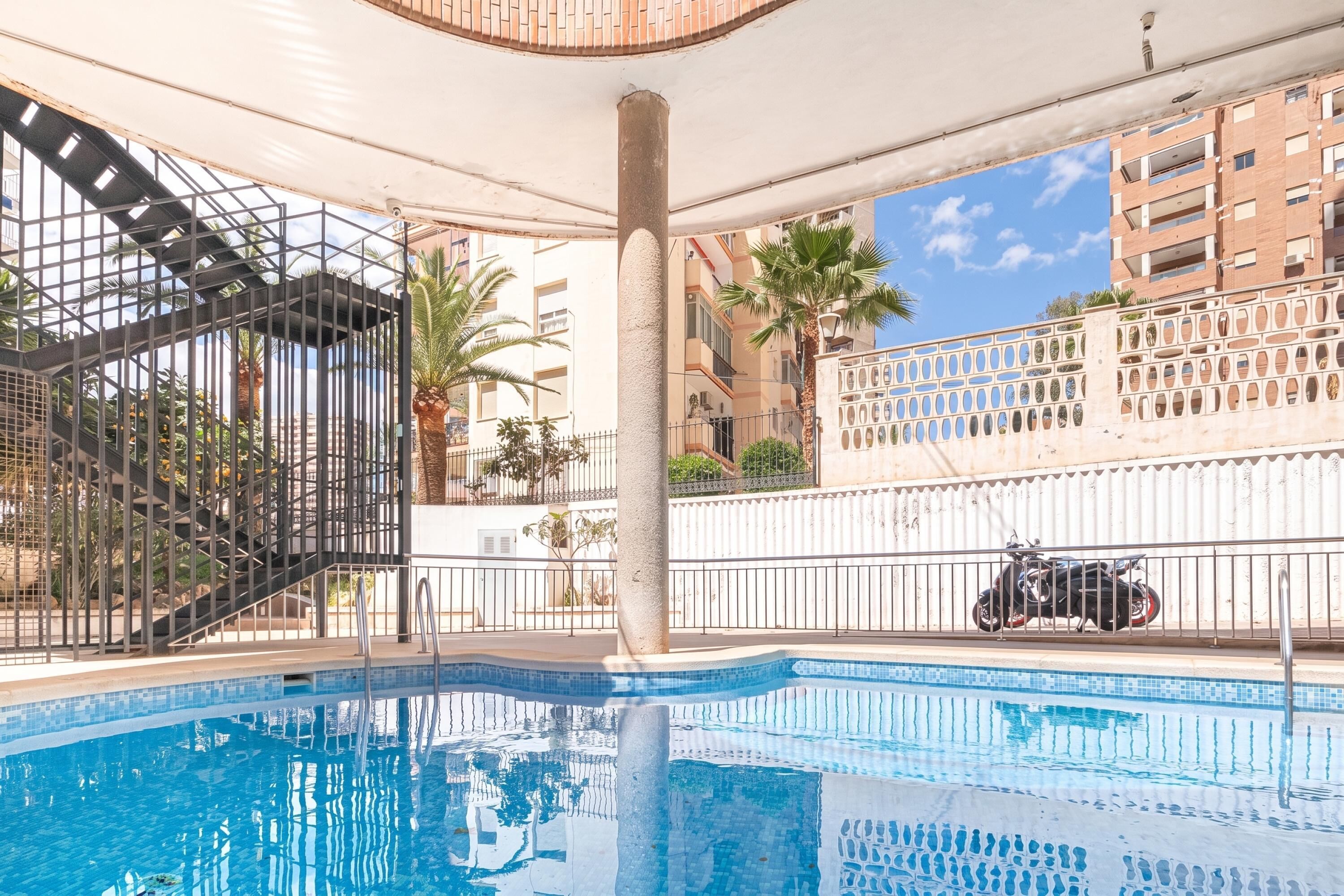 Una piscina interior con borde de azulejos, una escalera metálica y vistas de edificios circundantes.