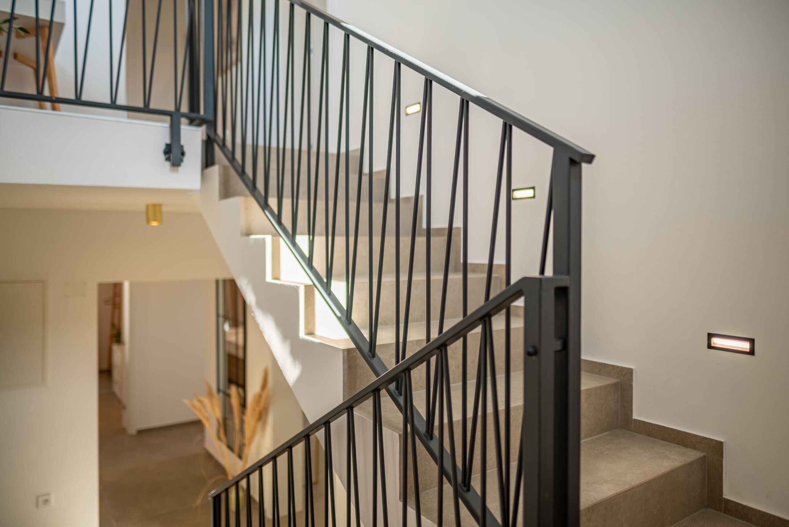 A modern staircase with a black metal railing and beige steps, leading to an upper floor.