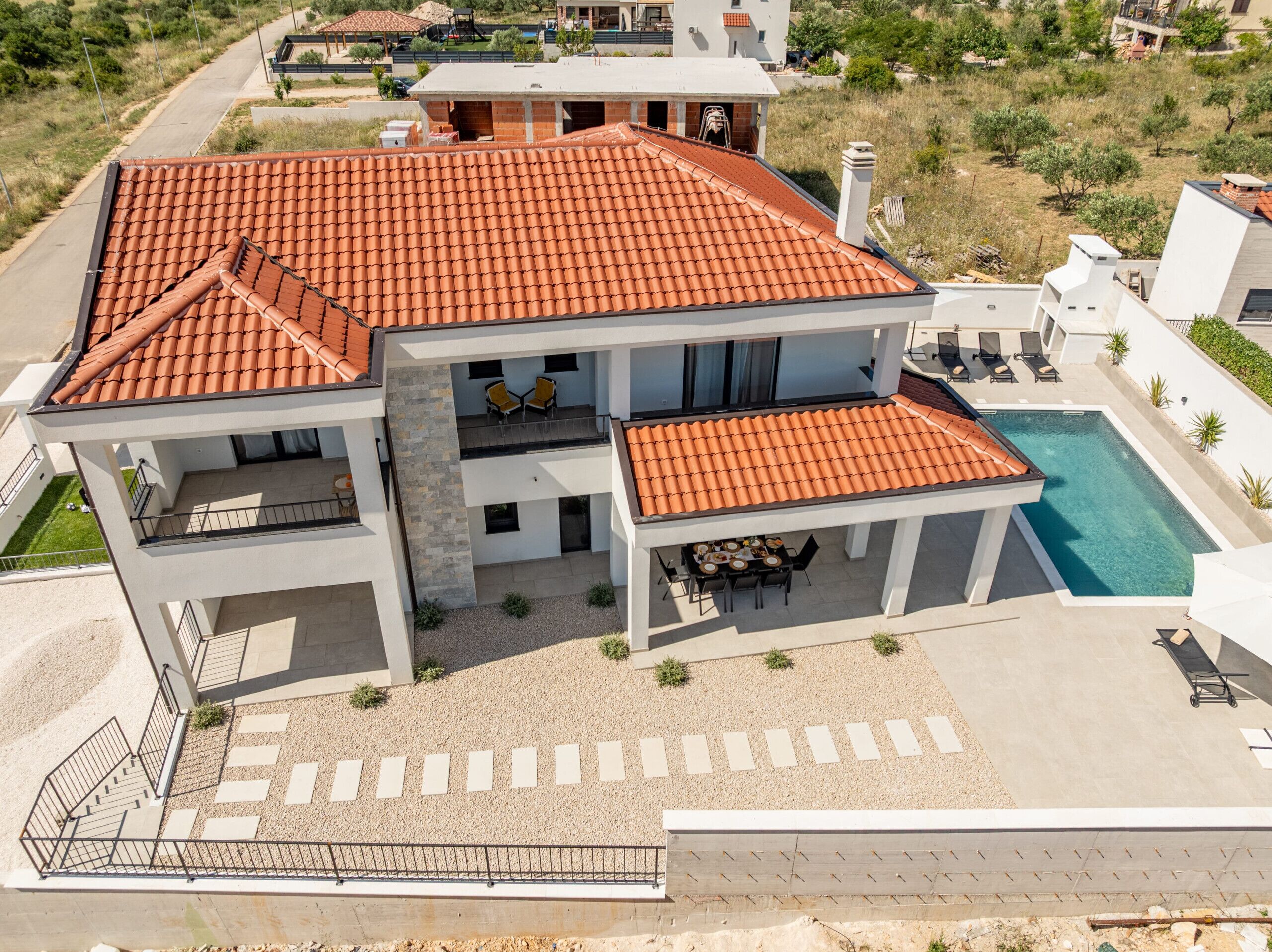 A two-story building with a tiled roof, a swimming pool, and outdoor seating.