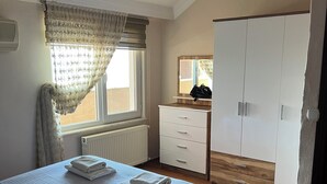 A bedroom with a bed, a dresser, a wardrobe, and a window with curtains. - Has Home Nozbart (Trabzon)