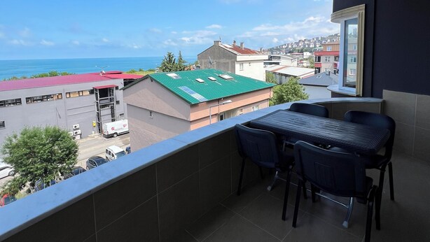 A balcony with a table and chairs, overlooking a residential area and the sea. - Has Home Nozbart (Trabzon)