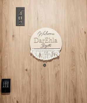 Eine Holztür mit einem Schild, auf dem 'Welcome DarEhla BogoTa' steht, und einem Zimmerschild mit der Nummer '402'.