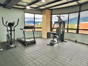 Ein Fitnessstudio mit Cardiogeräten, Gewichtstrainern und großen Fenstern mit Blick auf eine Stadtlandschaft.