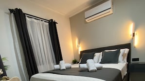 A hotel room with a bed, an air conditioning unit, and a nightstand.