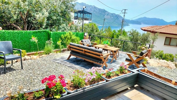 Une terrasse extérieure avec un banc en bois, un espace salon et des parterres de fleurs.