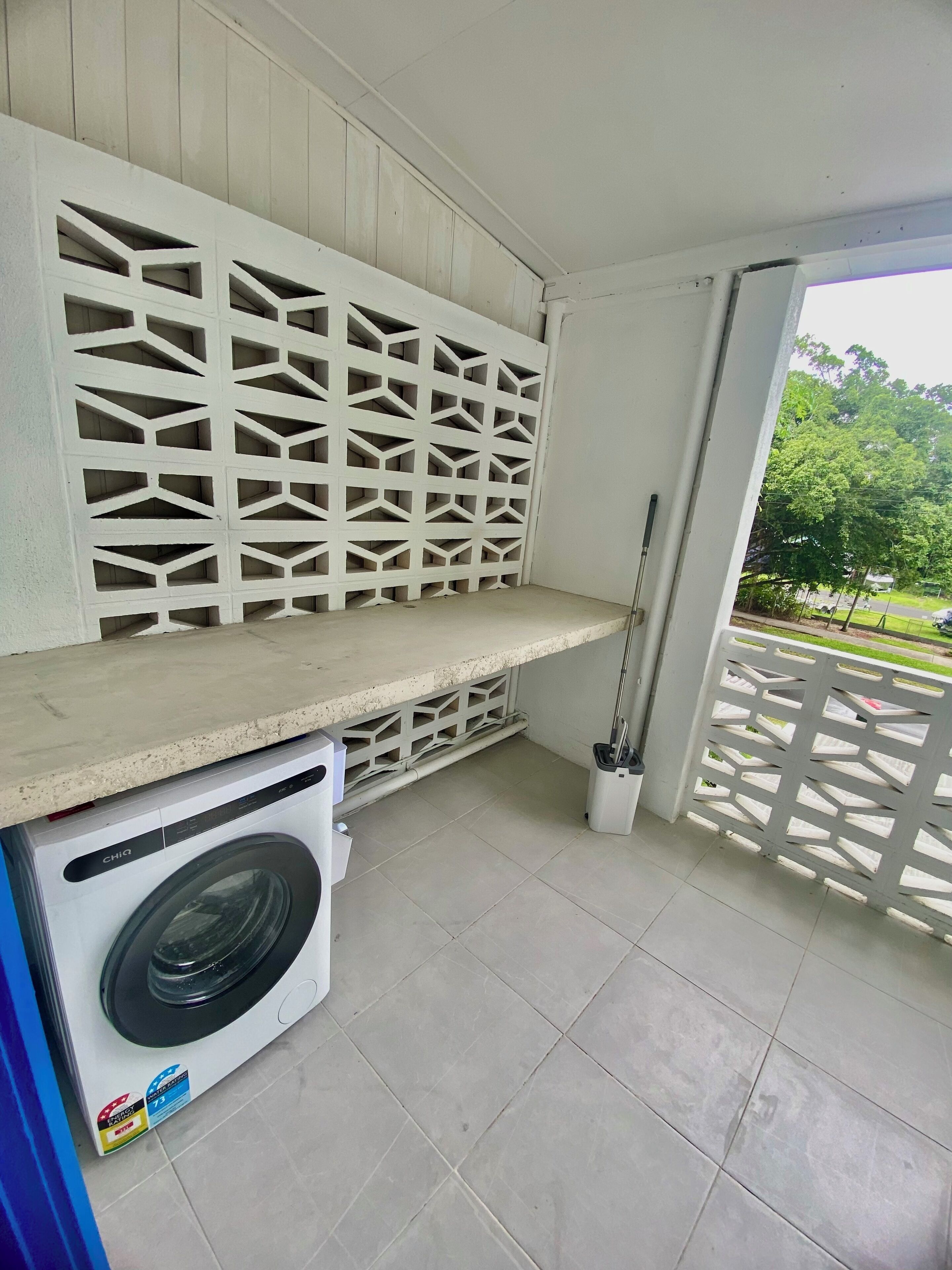 Un área de lavandería con lavadora, piso de baldosas y un panel blanco con diseño geométrico.