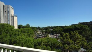 A view of a cityscape with a large building on the left and dense green trees in the foreground. - Nice studio with sea view balcony in Lignano Pineta (Lignano Sabbiadoro)