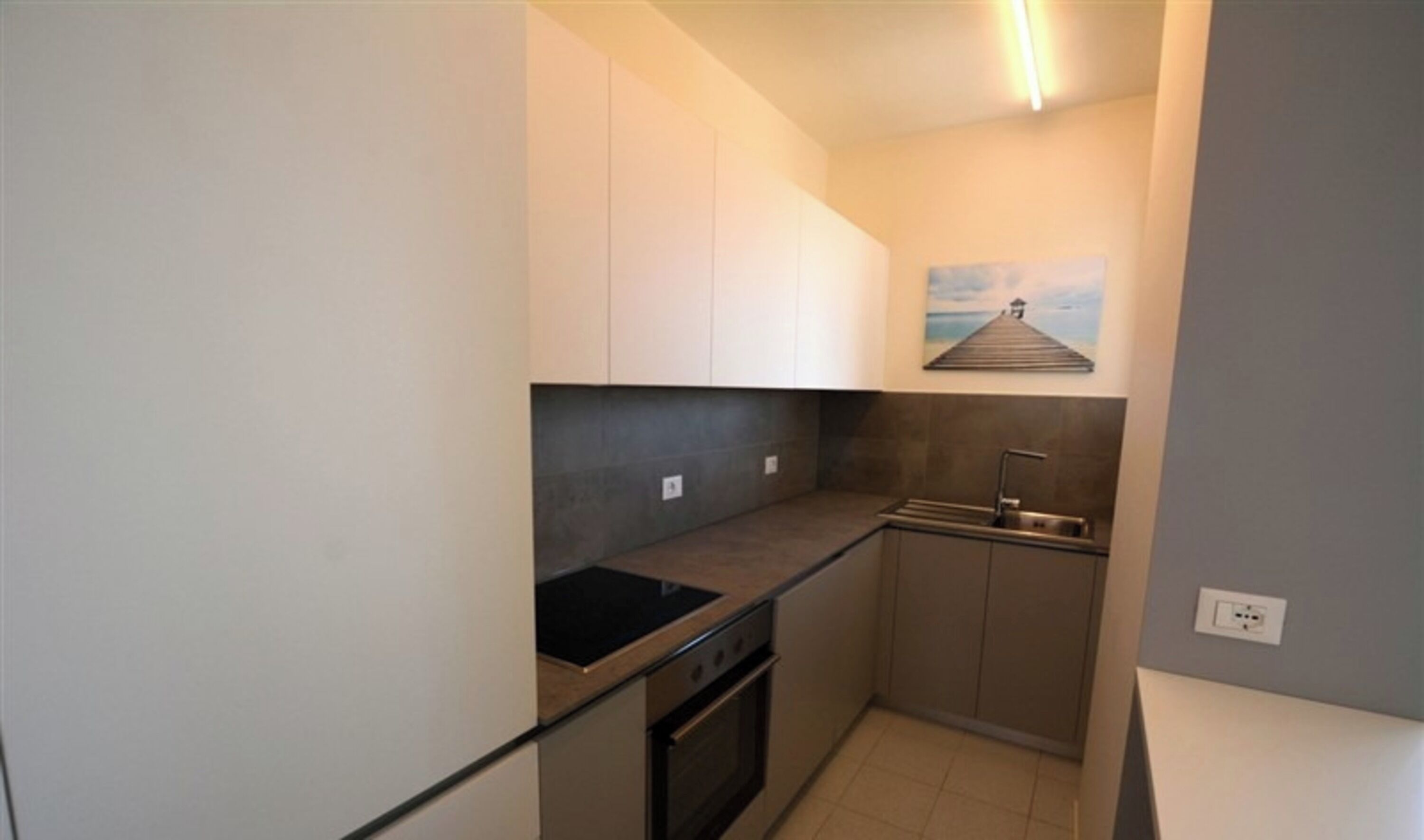 A compact kitchen with a black stove, a sink, and a painting of a pier on the wall.