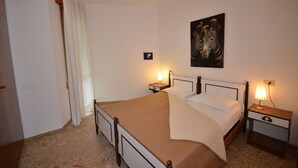 Une chambre d’hôtel avec un lit, deux tables de chevet avec des lampes, un tableau représentant une zèbre accroché au mur et une porte avec un rideau.