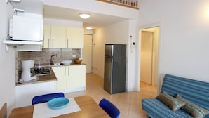 A compact kitchen with a stove, sink, and refrigerator, a dining area with a table and chairs, and a blue sofa in a living area. - Enjoy your vacation in style in Bibione (Bibione)
