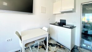 A small, modern kitchen with white cabinetry, a black countertop, and a flat-screen TV mounted on the wall. - DRAMA @ Danza Del Mar / for Adults - View, Heated pool, Hot tub, Fast WI-FI (Vir)