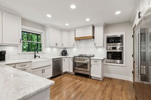 A modern kitchen with white cabinets, a wooden floor, a built-in oven, and a stainless steel refrigerator.