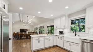 Una cocina moderna con armarios blancos, lavavajillas de acero inoxidable y una zona de comedor con mesa y sillas de madera.