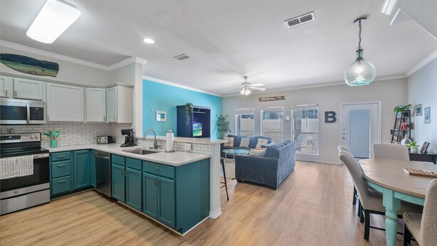 A modern kitchen with teal cabinets, a central island, and a dining area with a table and chairs. - Pet-Friendly Coastal Townhome | Heated Pool & Private Patio (Corpus Christi)
