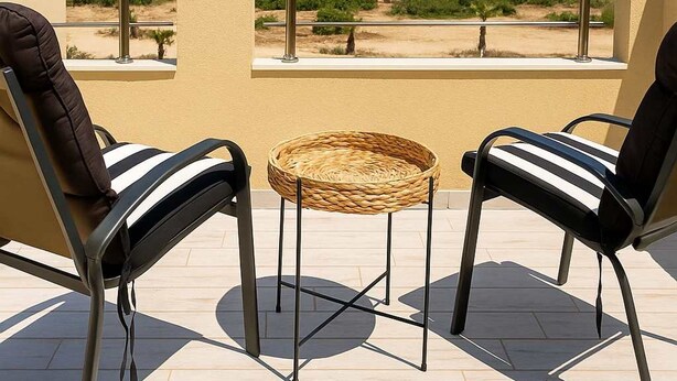A balcony with two chairs and a small table, overlooking a beach and ocean.