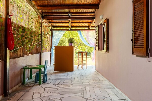 A corridor with a tiled floor, a green chair, a small table, a red bag, and a wooden door with a window.