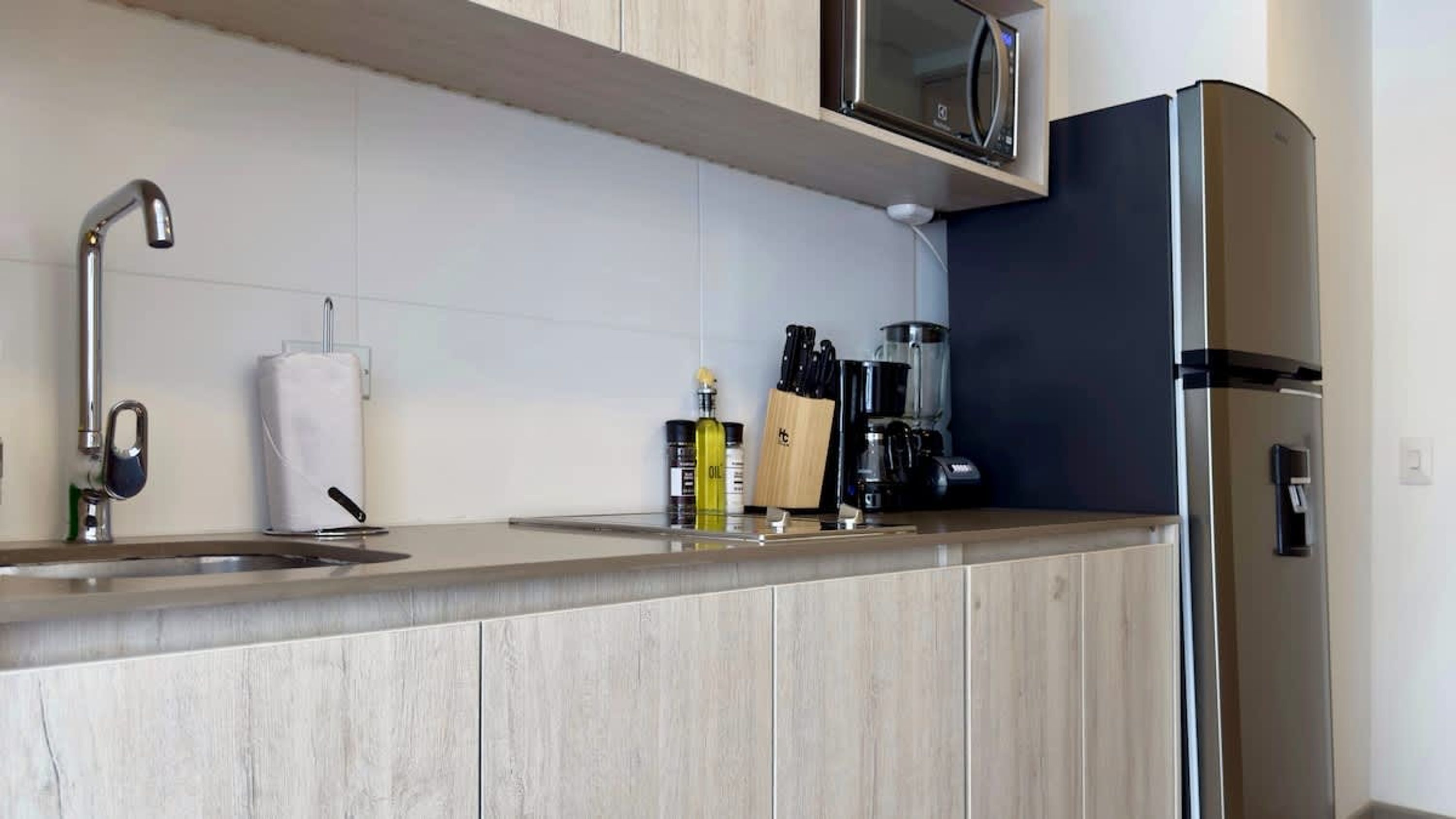 A modern kitchen with a stainless steel refrigerator, a microwave, a coffee maker, and a knife block.
