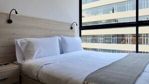 A modern bedroom with a large bed, two bedside tables, and a window with a view of a building.