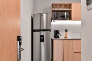 A compact kitchen with a stainless steel refrigerator, a microwave, and a coffee maker on the countertop.