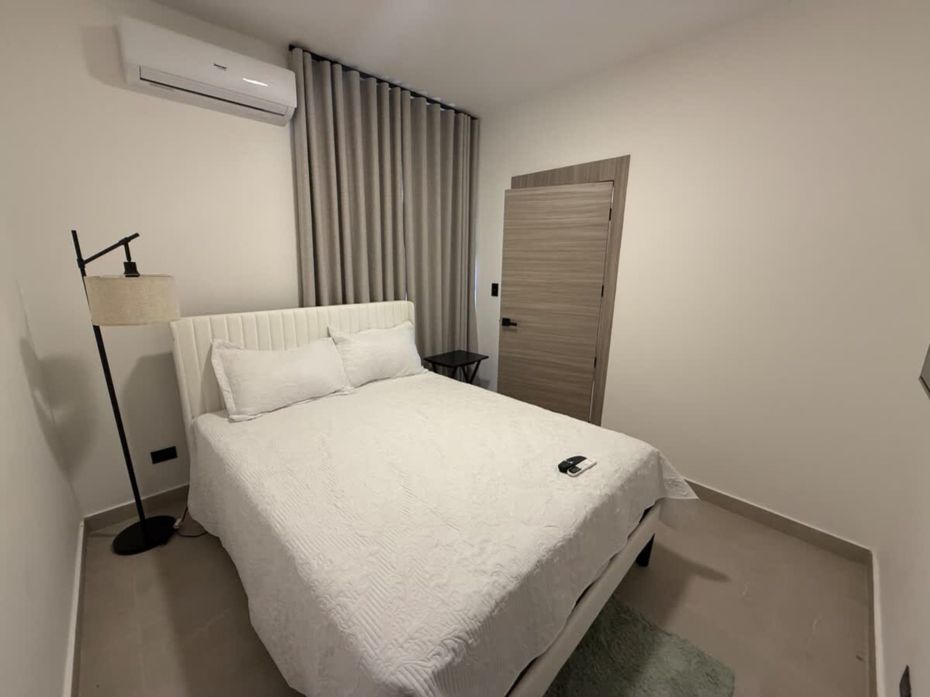 A neatly made bed with a white duvet, a bedside lamp, and a small table with a phone on it.