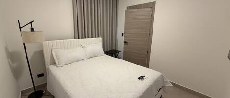 A neatly made bed with a white duvet, a bedside lamp, and a small table with a phone on it.