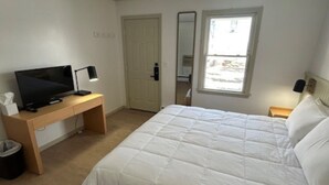 Een slaapkamer met een bed, een bureau met een computer, een prullenbak en een raam.