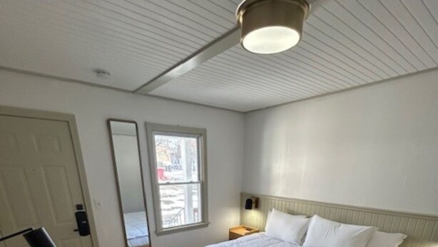 Een slaapkamer met een groot bed, nachtkastjes, een spiegel, een raam en een plafondlamp.